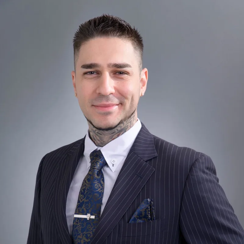 Carlos Lastres, photographed against a grey background in a navy pinstripe suit and patterned tie.